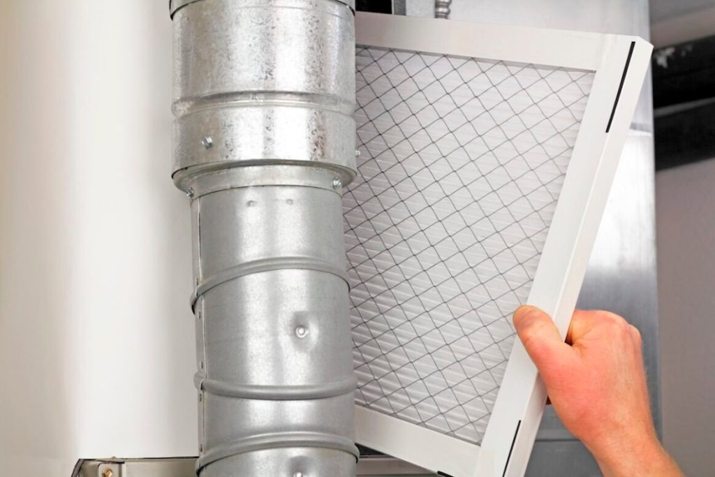 Male arm and hand replacing disposable air filter in residential air furnace.