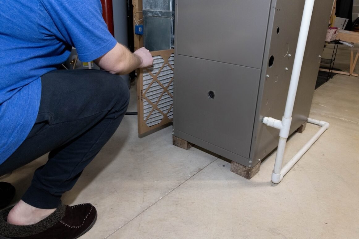 pulling old dirty furnace filter from heating unit in basement